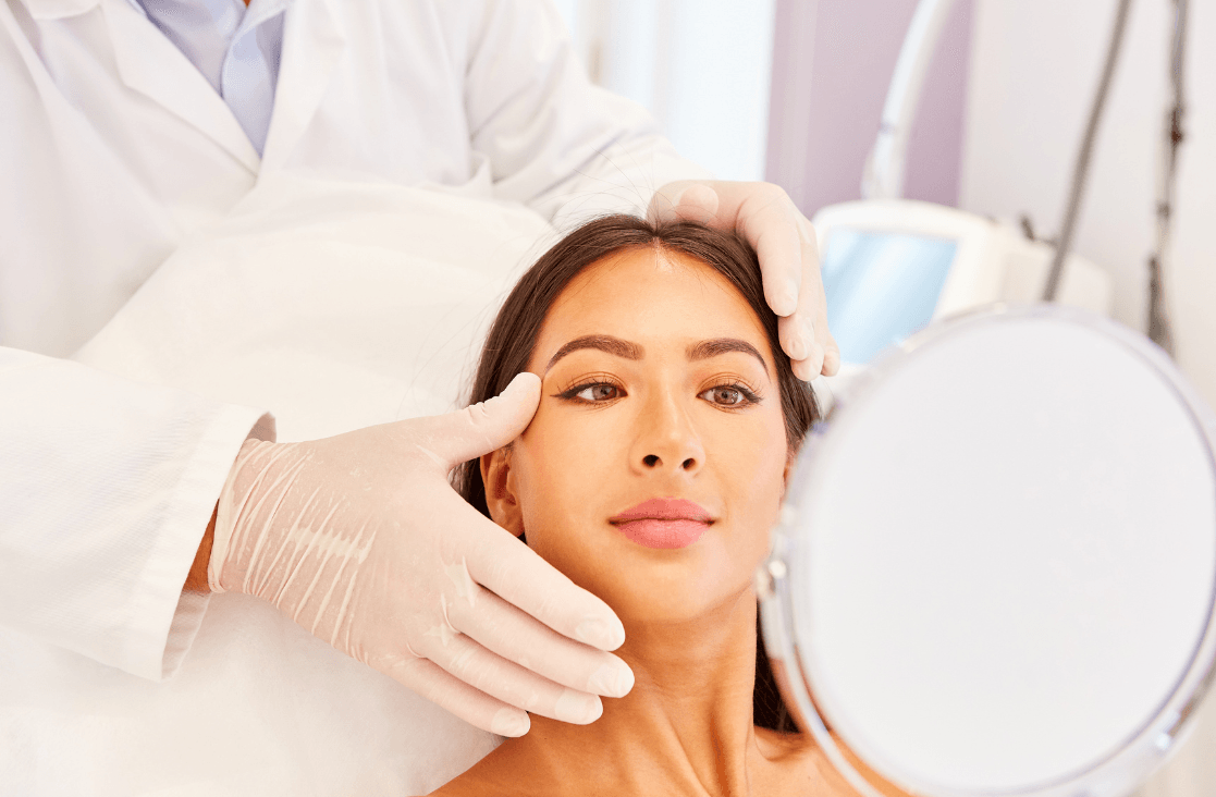 Facial Scar Treatment: woman at doctor's office looking into a mirror after procedure