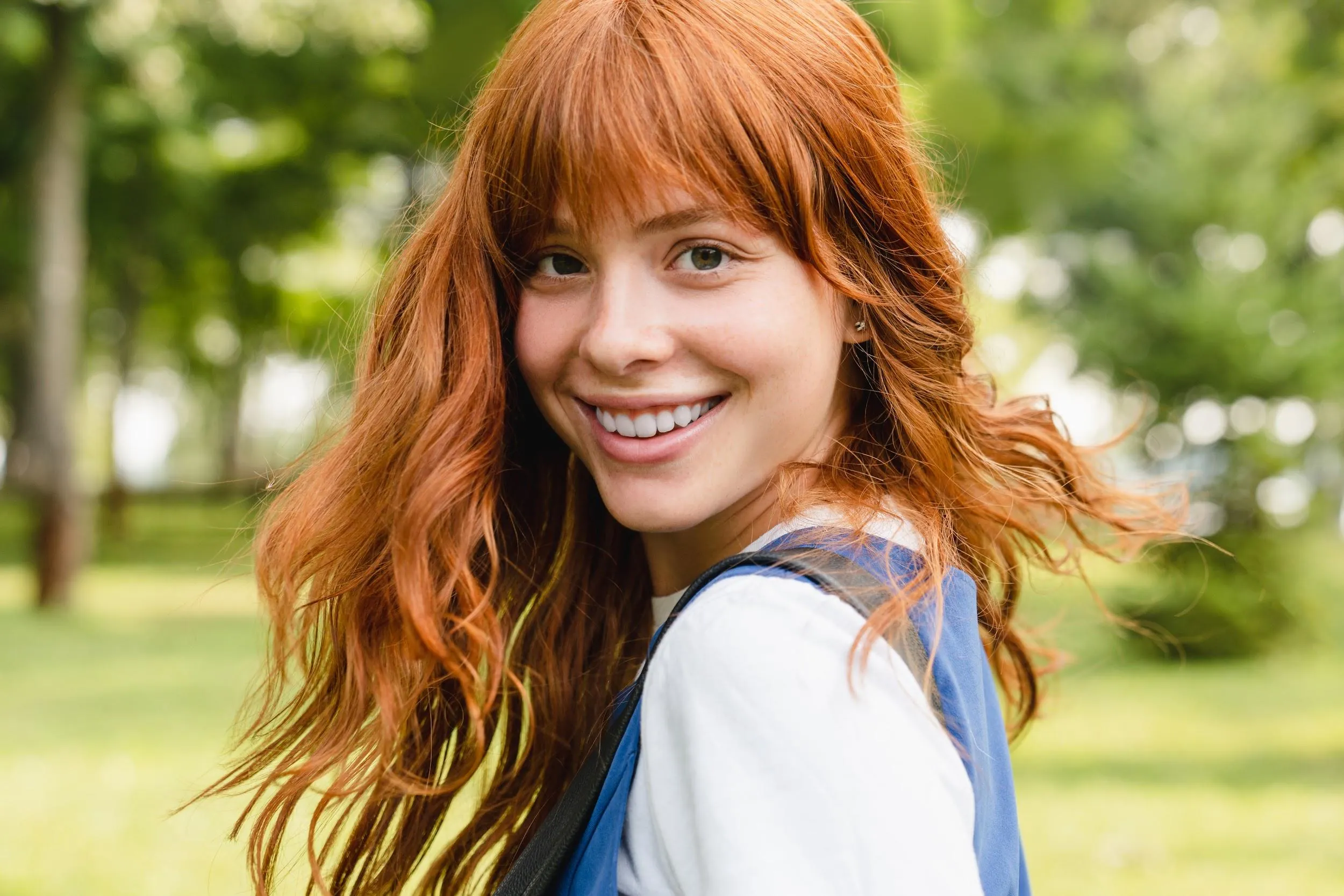 Teen rhinoplasty: Red-haired teenage girl smiling outdoors with natural profile and youthful facial balance