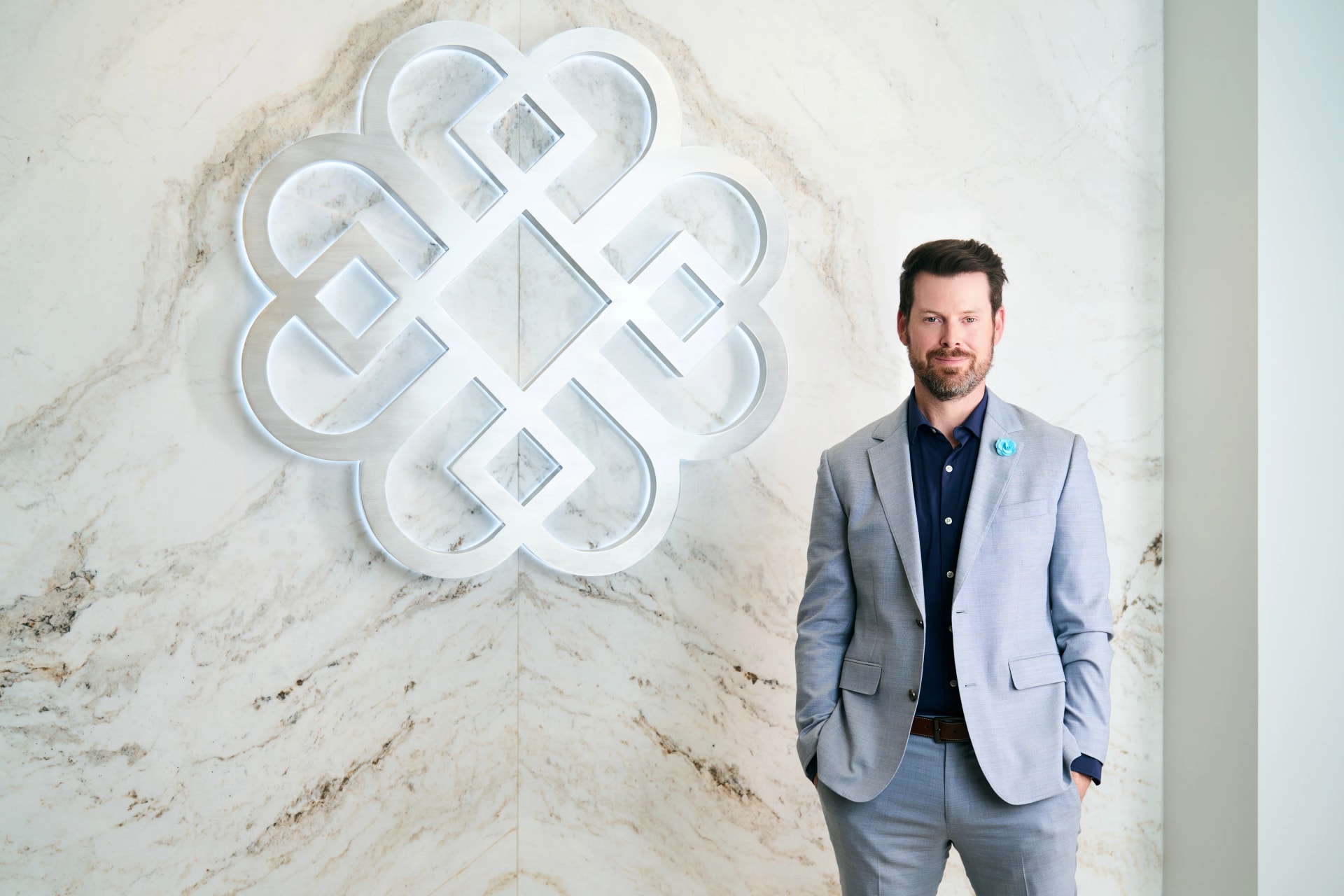Plastic surgeon standing in modern clinic lobby with marble wall and decorative logo background