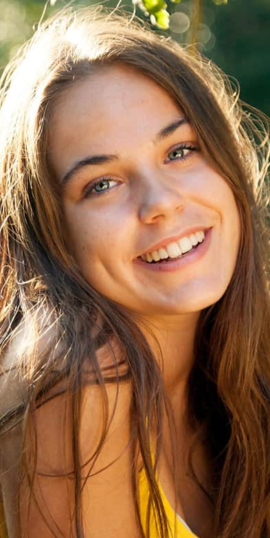 Teen rhinoplasty: Smiling teenage girl outdoors with natural facial features and confident expression