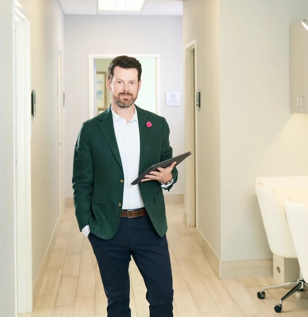 Teen rhinoplasty: Surgeon walking through a modern clinic hallway holding a tablet during teen care visit