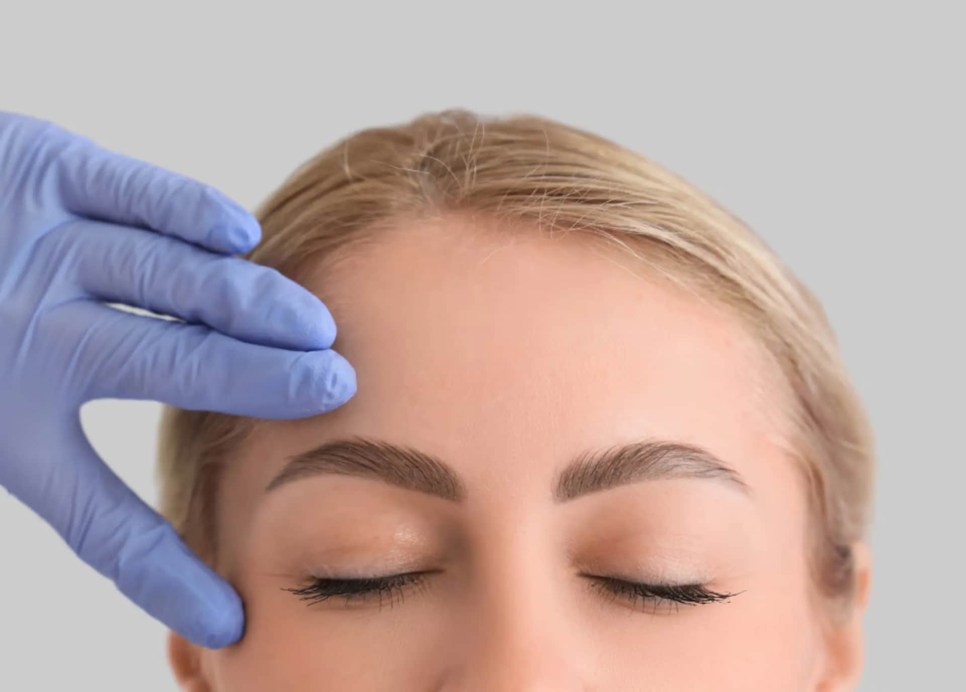 Ethnic Rhinoplasty in Plano TX: Woman with eyes closed while gloved hand analyzes her eyebrows
